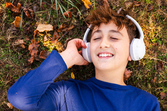 A boy lying down in the grass listening to music on headphones