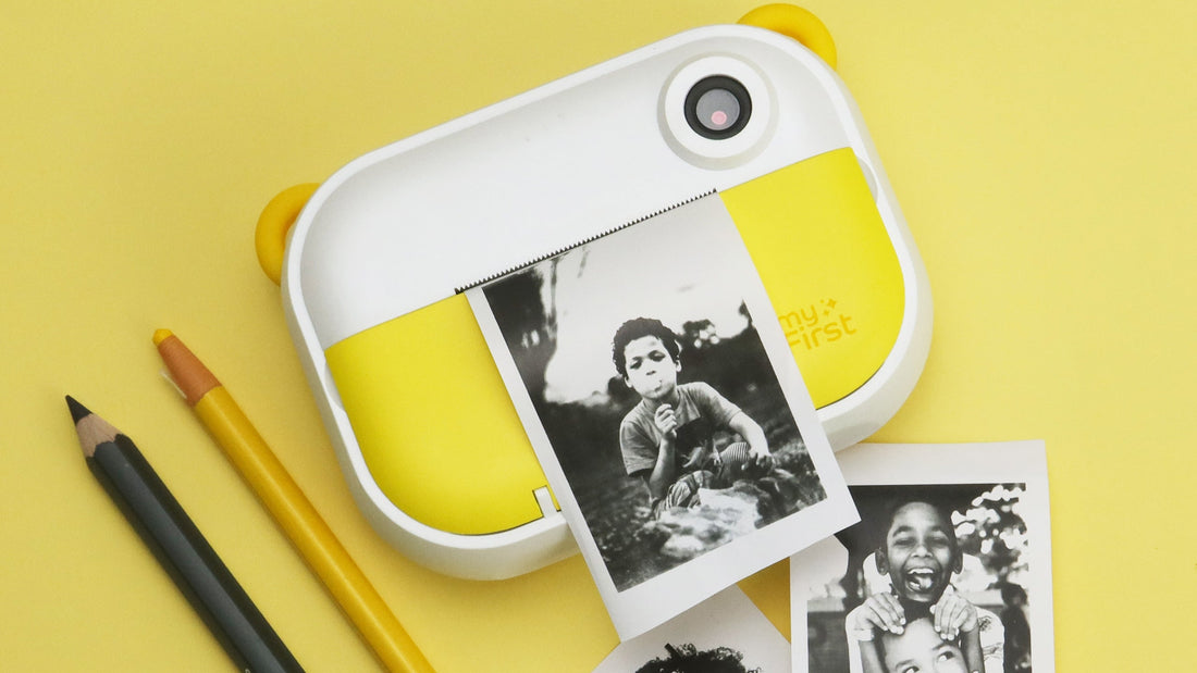 The myFirst Insta 2 printing out a photo of a boy, while resting on a yellow background next to pencils