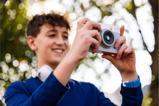 A young man holding a gray and white camera outside