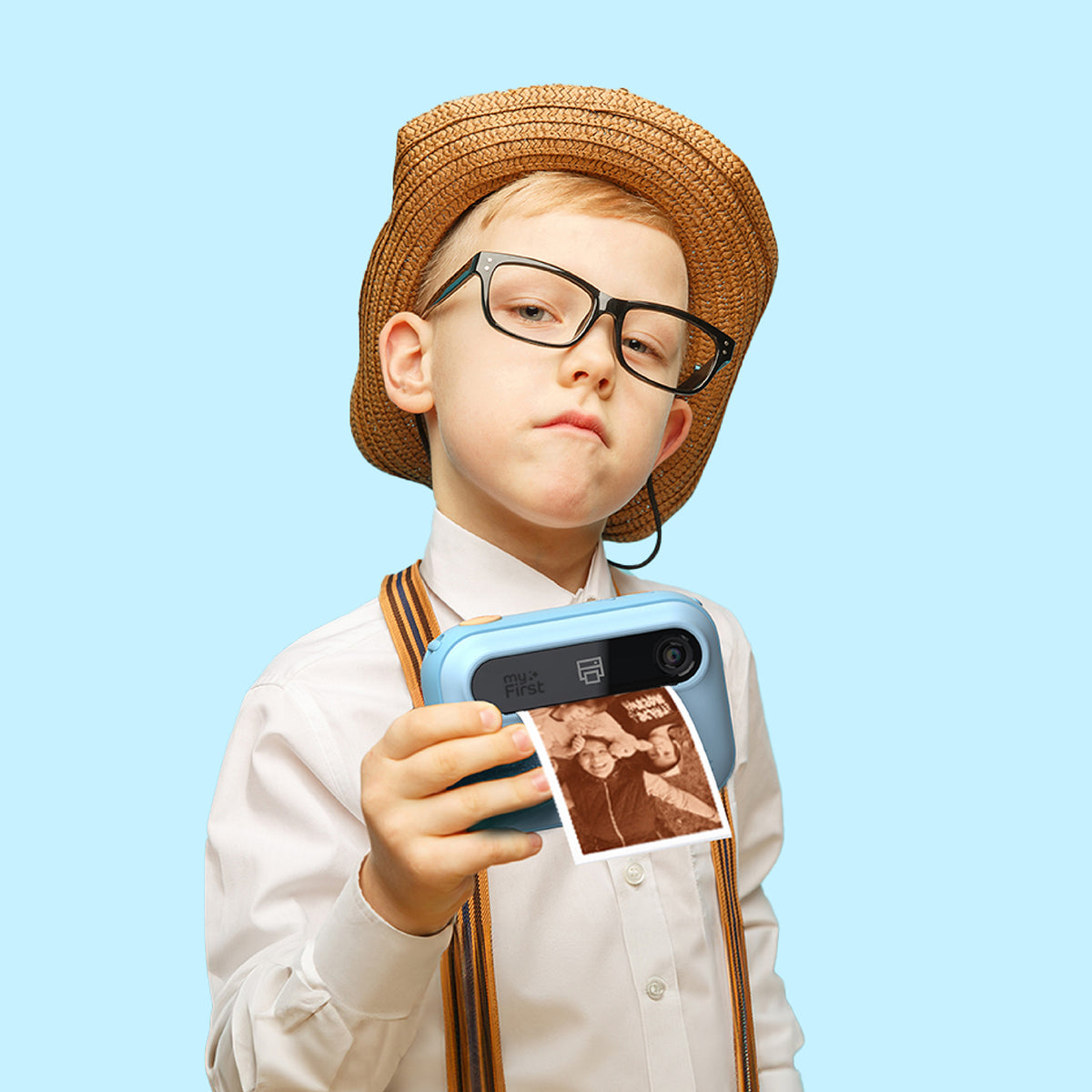 myFirst Insta 20 blue kids instant print camera held by a boy aged 6 to 8 wearing a straw hat and glasses, showing a printed photo.