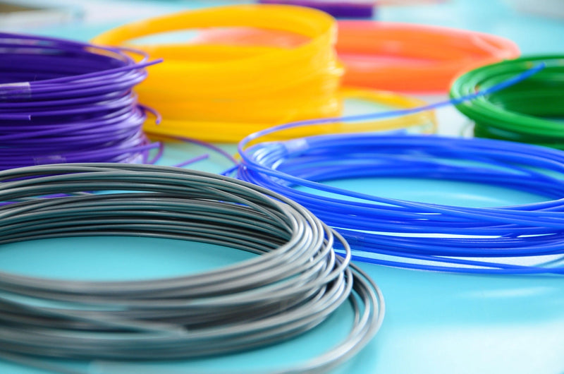 myFirst 3D pen PCL filament coils in vibrant colors like purple, orange, blue, and green, on a light blue background.