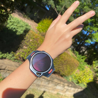 myFirst Fone R2 dark navy kids smartwatch worn on a hand making a peace sign in a sunny outdoor garden setting.
