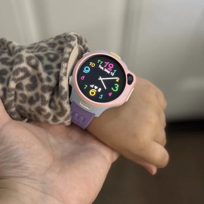 myFirst Fone R2 pink and purple kids smartwatch worn on a child's wrist indoors, displaying a colorful analog and digital watch face